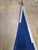 A close-up of a blue triangular fabric panel with white stitched trim and a metal ring attachment, laid on a concrete floor.